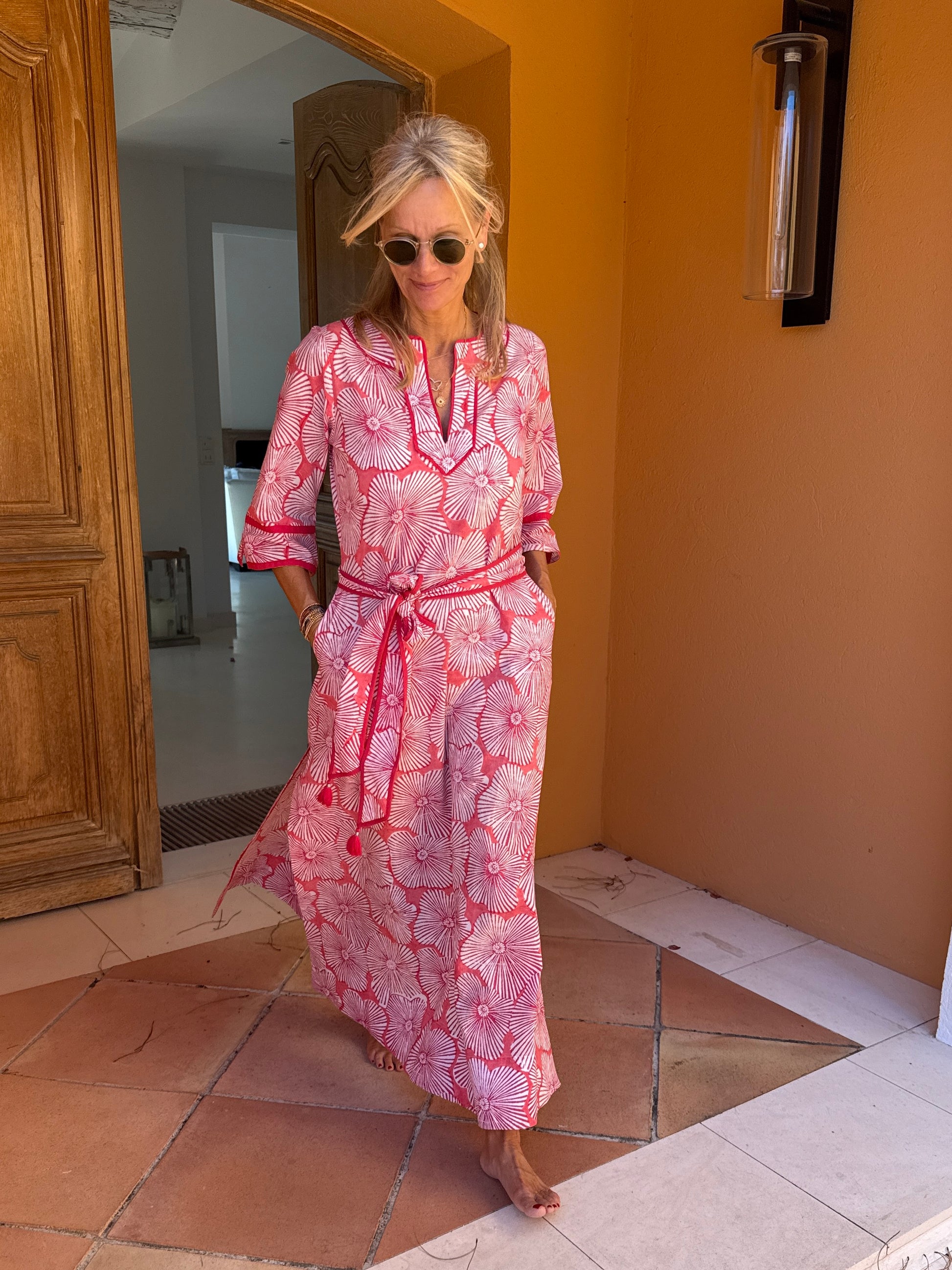 Woman in a pink patterned dress standing in a doorway.